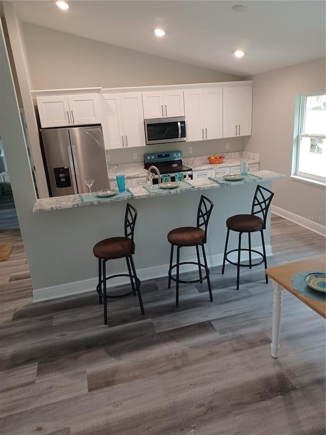 kitchen featuring a kitchen bar, dark wood-type flooring, appliances with stainless steel finishes, light stone counters, and white cabinetry