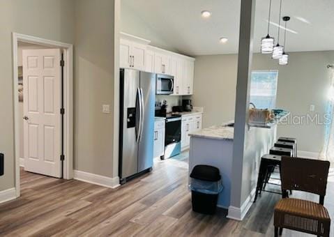 kitchen featuring stainless steel appliances, white cabinets, hardwood / wood-style floors, hanging light fixtures, and lofted ceiling