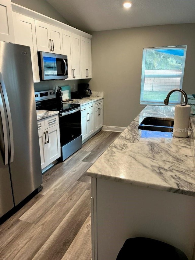 kitchen featuring light stone counters, stainless steel appliances, sink, light hardwood / wood-style floors, and white cabinetry