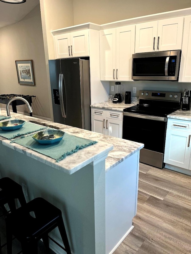 kitchen featuring stainless steel appliances, light stone counters, light hardwood / wood-style flooring, a breakfast bar area, and white cabinets