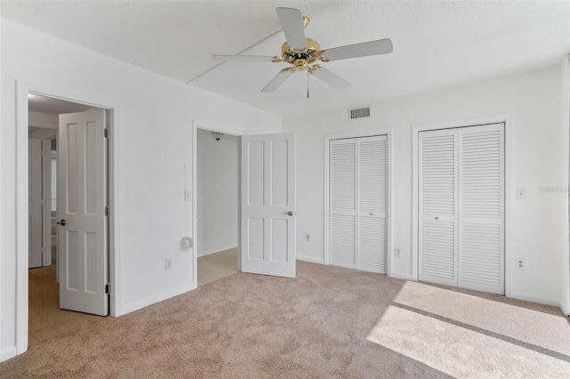 unfurnished bedroom featuring light colored carpet, two closets, ceiling fan, and a textured ceiling