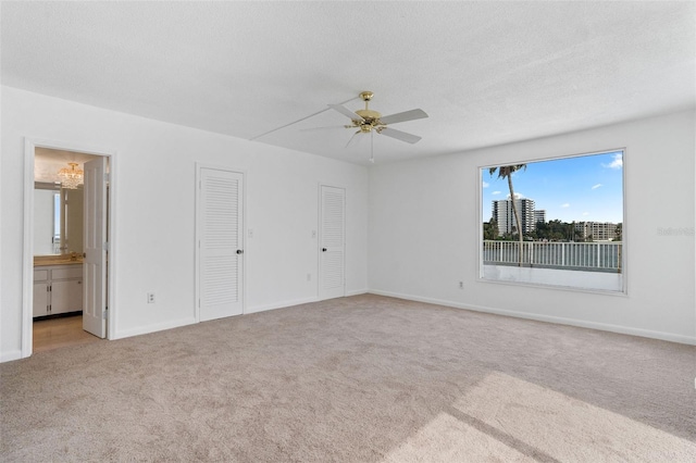 unfurnished bedroom with a textured ceiling, light carpet, connected bathroom, two closets, and ceiling fan