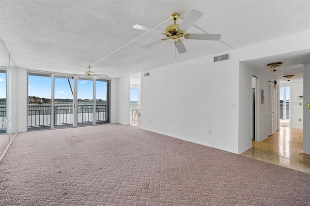 carpeted empty room featuring a wall of windows, ceiling fan, and a textured ceiling