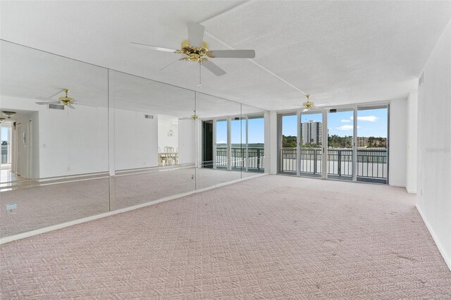 carpeted spare room with ceiling fan, expansive windows, and a textured ceiling