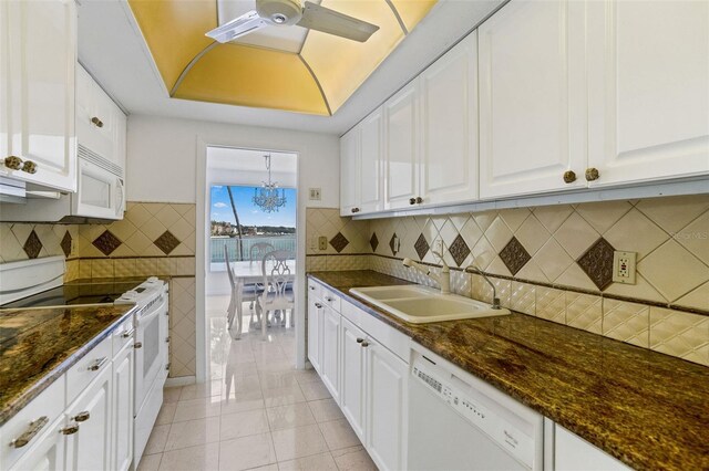 kitchen featuring dark stone countertops, ceiling fan with notable chandelier, white appliances, white cabinetry, and sink