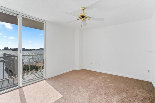 carpeted spare room with a water view, ceiling fan, and a wall of windows