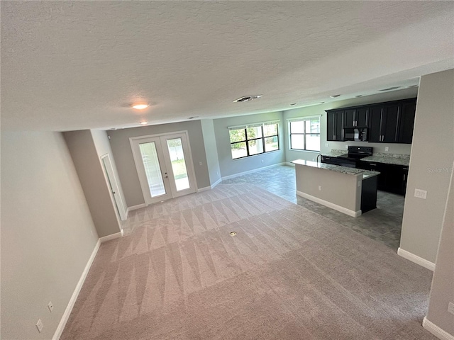 unfurnished living room with a textured ceiling, light colored carpet, and french doors