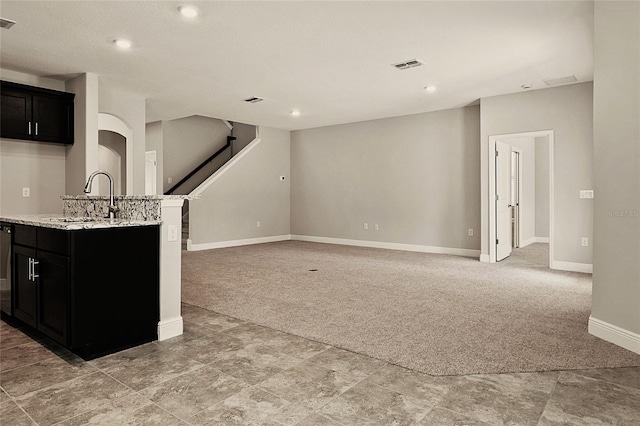 kitchen with dishwasher, a kitchen island with sink, light colored carpet, light stone counters, and sink