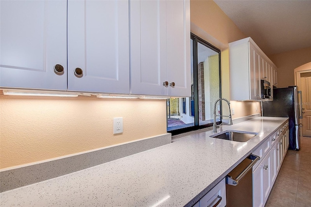 kitchen with appliances with stainless steel finishes, white cabinetry, sink, light tile patterned floors, and light stone counters