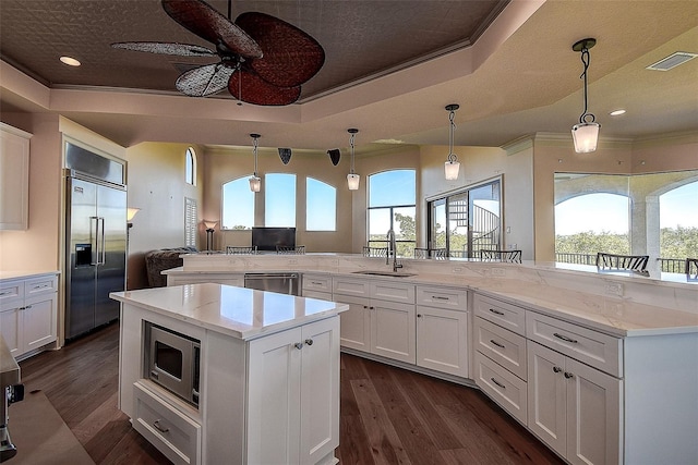 kitchen featuring sink, built in appliances, a tray ceiling, ornamental molding, and white cabinets