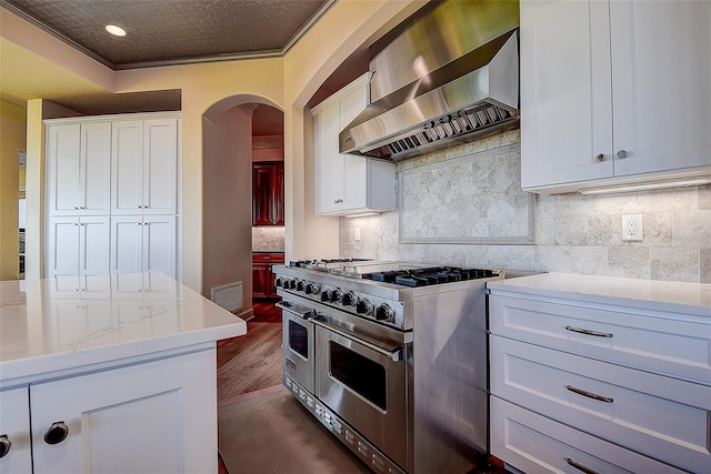 kitchen featuring dark wood-type flooring, wall chimney exhaust hood, crown molding, white cabinetry, and range with two ovens