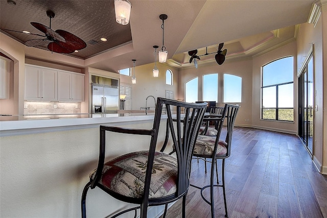 kitchen with pendant lighting, wood-type flooring, white cabinets, a raised ceiling, and stainless steel built in fridge