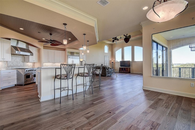 kitchen featuring decorative light fixtures, premium appliances, an island with sink, wall chimney range hood, and white cabinets