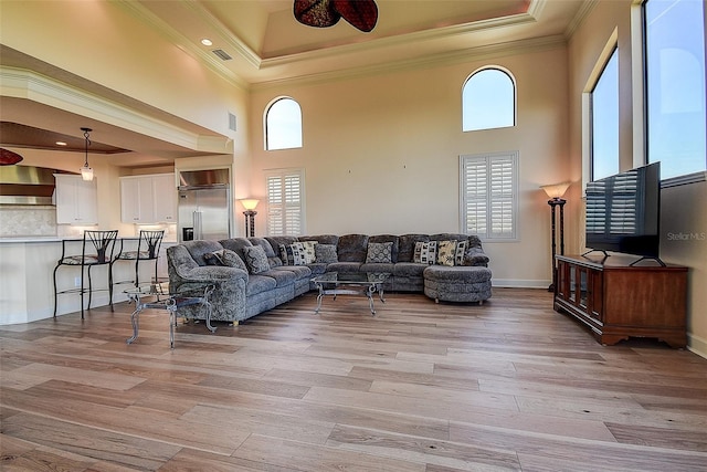 living room featuring a towering ceiling, ornamental molding, and light wood-type flooring