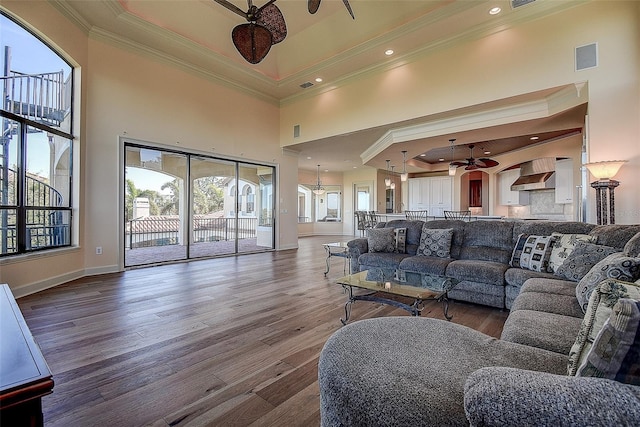 living room with hardwood / wood-style flooring, a towering ceiling, ceiling fan, and a tray ceiling