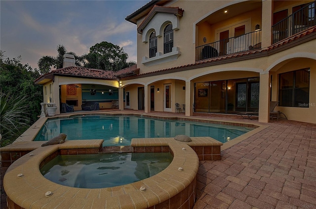 pool at dusk featuring an in ground hot tub and a patio