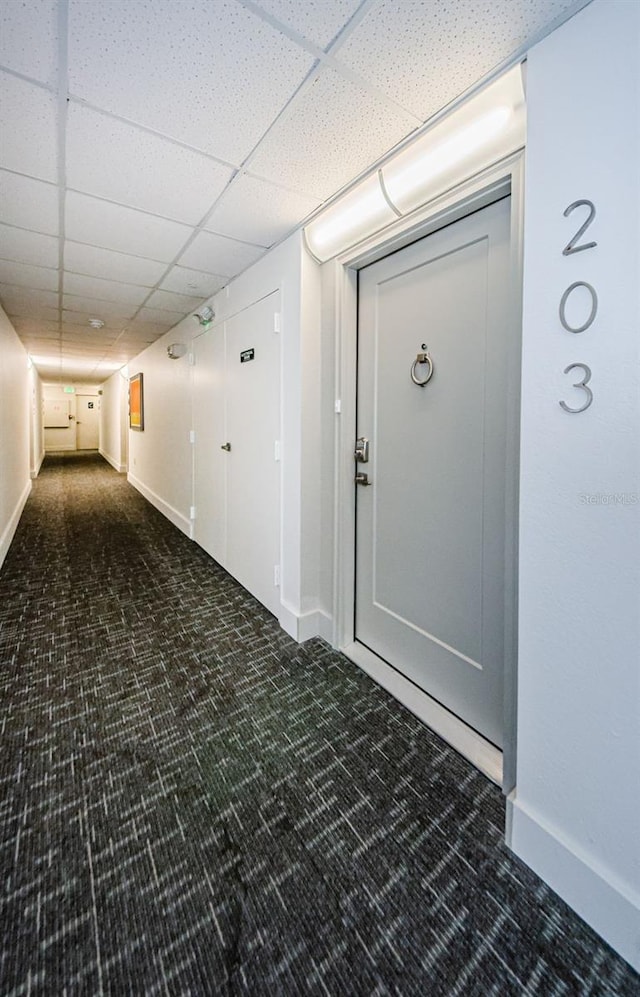 hallway featuring dark colored carpet and a paneled ceiling