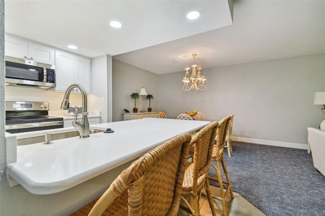 kitchen with a chandelier, stainless steel appliances, a kitchen bar, dark carpet, and white cabinets