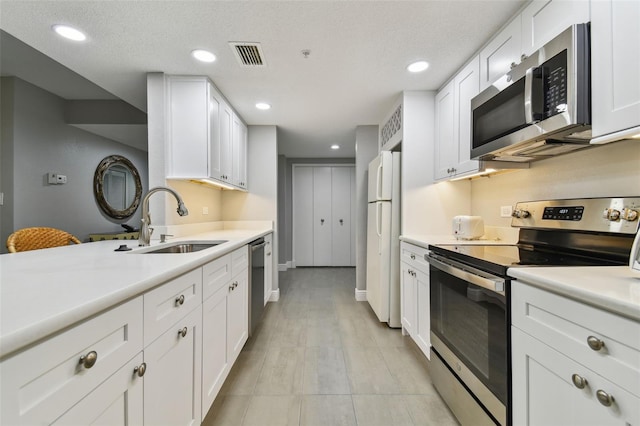 kitchen featuring sink, light tile floors, white cabinets, appliances with stainless steel finishes, and a textured ceiling