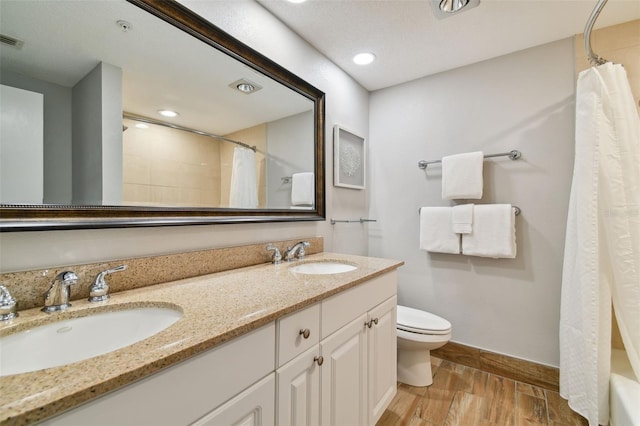 full bathroom with toilet, hardwood / wood-style flooring, shower / bath combo, double sink, and vanity with extensive cabinet space