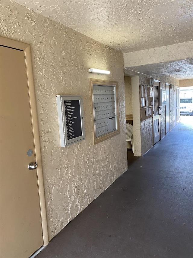 hall with mail area, a textured ceiling, and a textured wall