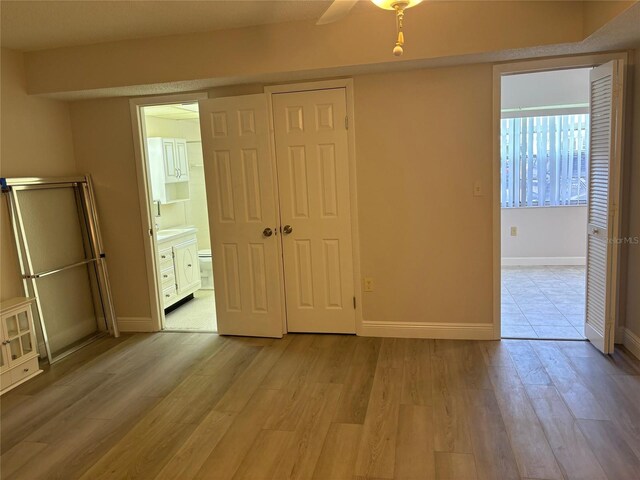 unfurnished bedroom featuring connected bathroom, light hardwood / wood-style flooring, ceiling fan, and a closet