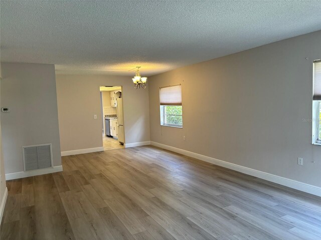 empty room featuring a textured ceiling, an inviting chandelier, and hardwood / wood-style flooring