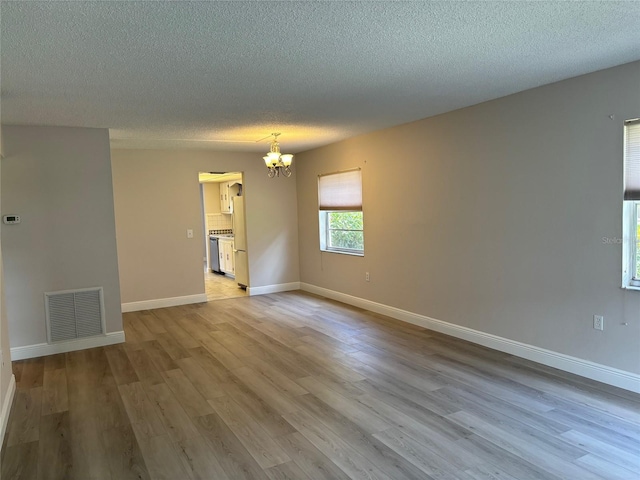 empty room featuring light wood-type flooring, an inviting chandelier, baseboards, and visible vents