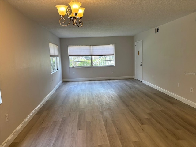 unfurnished room featuring hardwood / wood-style floors, a textured ceiling, and a chandelier