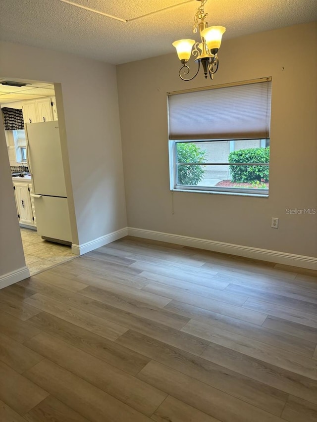 spare room with light wood-type flooring, a textured ceiling, baseboards, and a notable chandelier