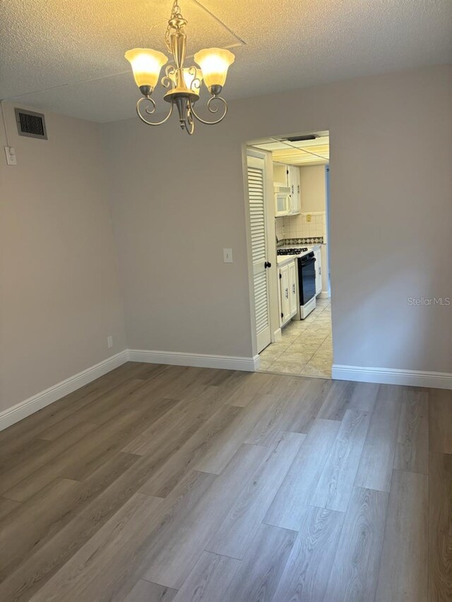 unfurnished room featuring a textured ceiling, light wood-type flooring, and a chandelier