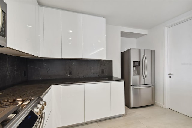 kitchen with light tile floors, appliances with stainless steel finishes, white cabinets, backsplash, and dark stone countertops