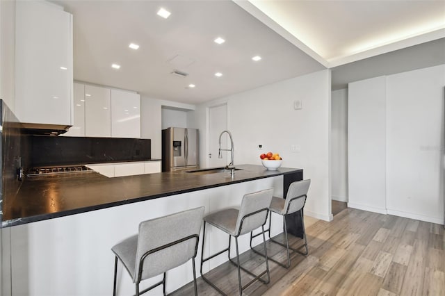 kitchen with a kitchen breakfast bar, light hardwood / wood-style floors, sink, stainless steel appliances, and white cabinets