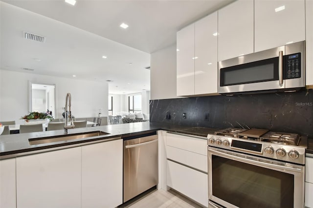 kitchen featuring backsplash, sink, stainless steel appliances, dark stone countertops, and white cabinets