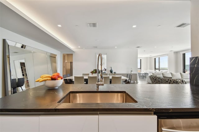 kitchen featuring white cabinetry, an island with sink, sink, and dark stone counters