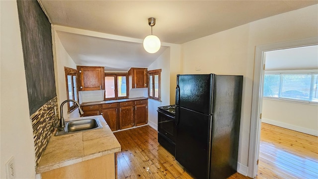 kitchen with range with electric cooktop, black refrigerator, pendant lighting, sink, and light hardwood / wood-style flooring