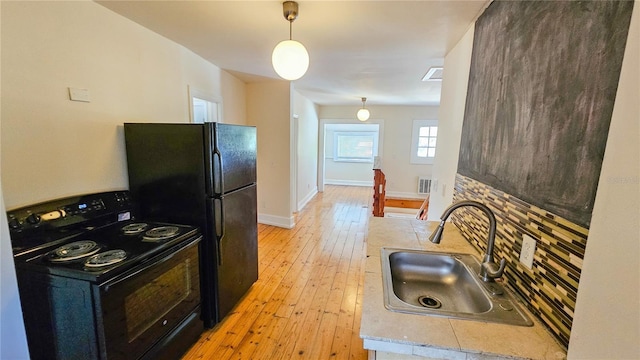 kitchen featuring hanging light fixtures, sink, light hardwood / wood-style floors, and black appliances