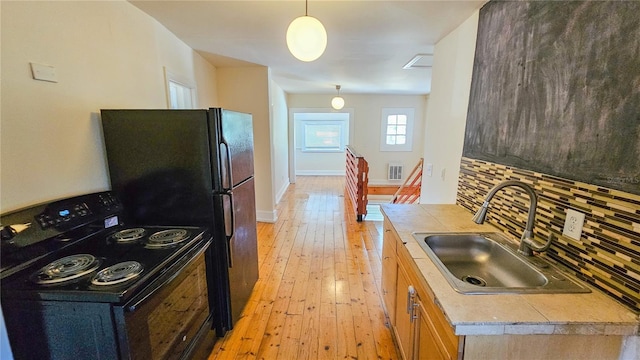 kitchen featuring sink, backsplash, black appliances, light hardwood / wood-style floors, and decorative light fixtures