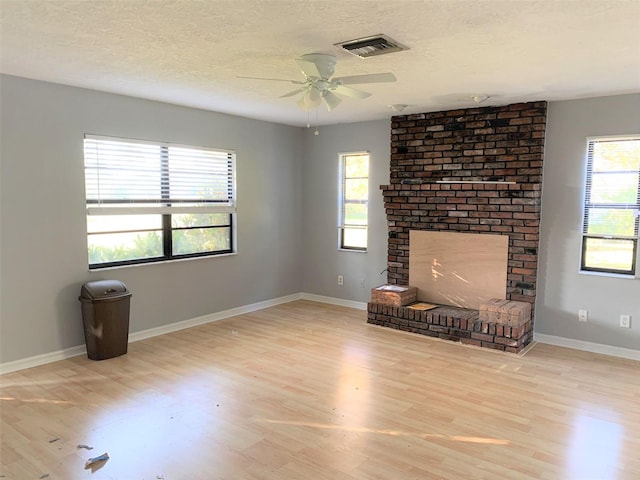 unfurnished living room with ceiling fan, a fireplace, light hardwood / wood-style floors, and a textured ceiling