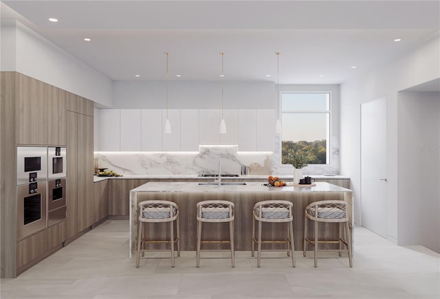 kitchen featuring white cabinets, oven, hanging light fixtures, and an island with sink