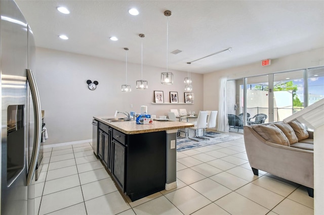 kitchen featuring hanging light fixtures, light stone counters, stainless steel appliances, sink, and a kitchen island with sink