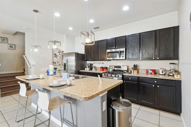 kitchen with decorative light fixtures, light tile patterned floors, a kitchen island with sink, a breakfast bar, and stainless steel appliances