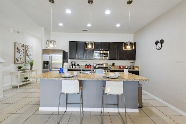 kitchen featuring appliances with stainless steel finishes, pendant lighting, a center island with sink, and a breakfast bar