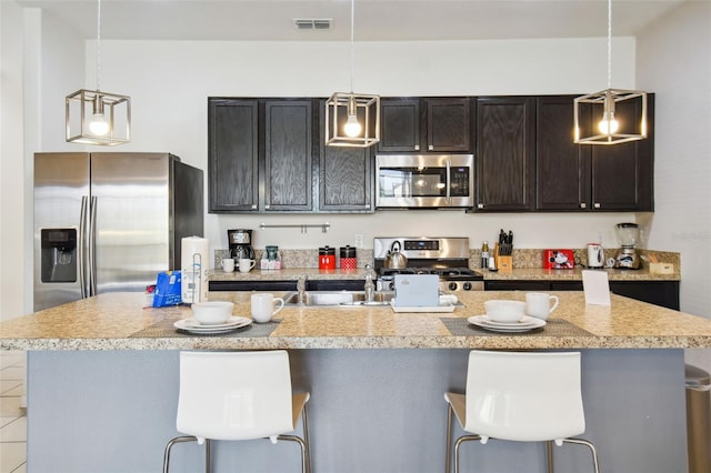 kitchen with an island with sink, hanging light fixtures, a breakfast bar area, and appliances with stainless steel finishes