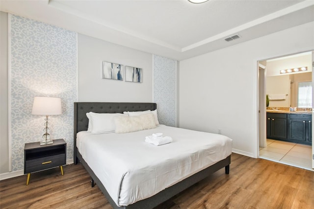 bedroom with connected bathroom, hardwood / wood-style floors, and a tray ceiling