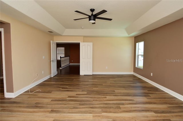 empty room with ceiling fan, wood-type flooring, and a raised ceiling