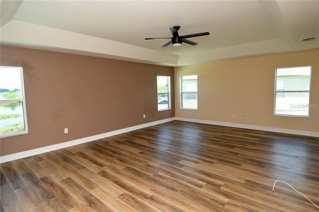 empty room with ceiling fan, a tray ceiling, and dark wood-type flooring