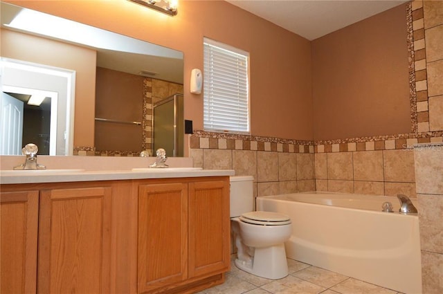 bathroom with toilet, dual bowl vanity, tile floors, and a bath to relax in