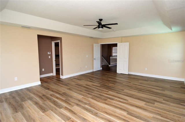 empty room with a raised ceiling, hardwood / wood-style floors, and ceiling fan