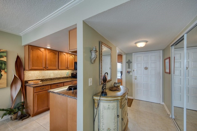 kitchen with light tile patterned flooring, tasteful backsplash, dark stone counters, ornamental molding, and a textured ceiling